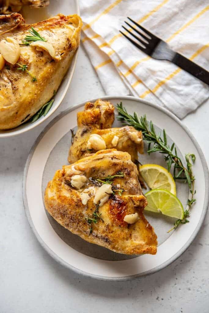 Garlic Herb chicken breast on a plate with lime slices a sprig of rosemary alongside. 