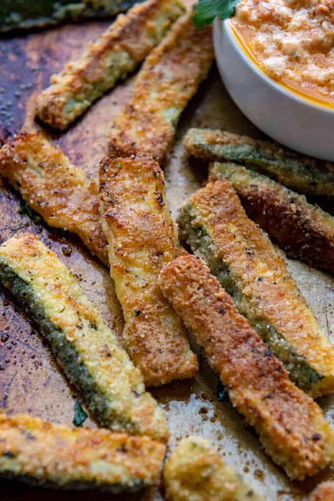 zucchini fries on a baking sheet with a dipping sauce in a bowl alongside. 