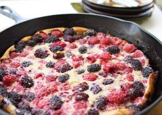 a cast iron skillet of mixed berry dutch baby ready to serve. 