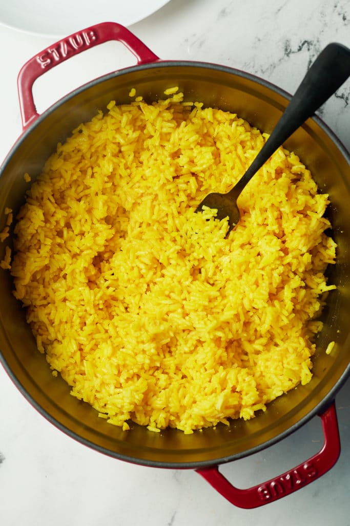 Dutch oven with yellow rice and a fork stuck in it.