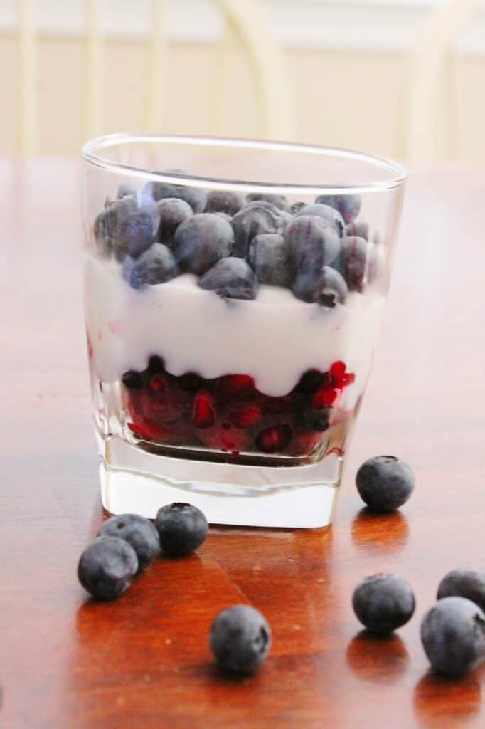 A single glass serving of red white and blue partfait with whole blueberries on the side. 