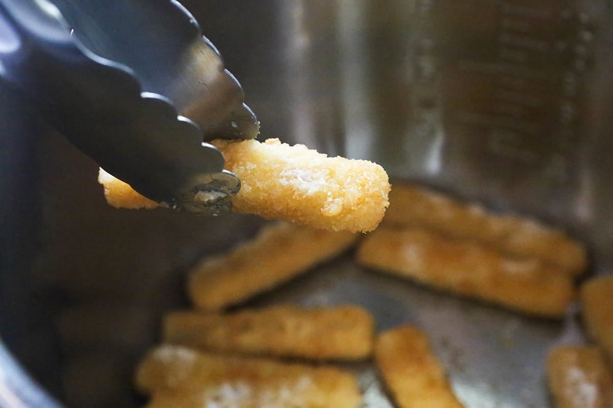 Tongs lifting a fish stick out of an air fryer.