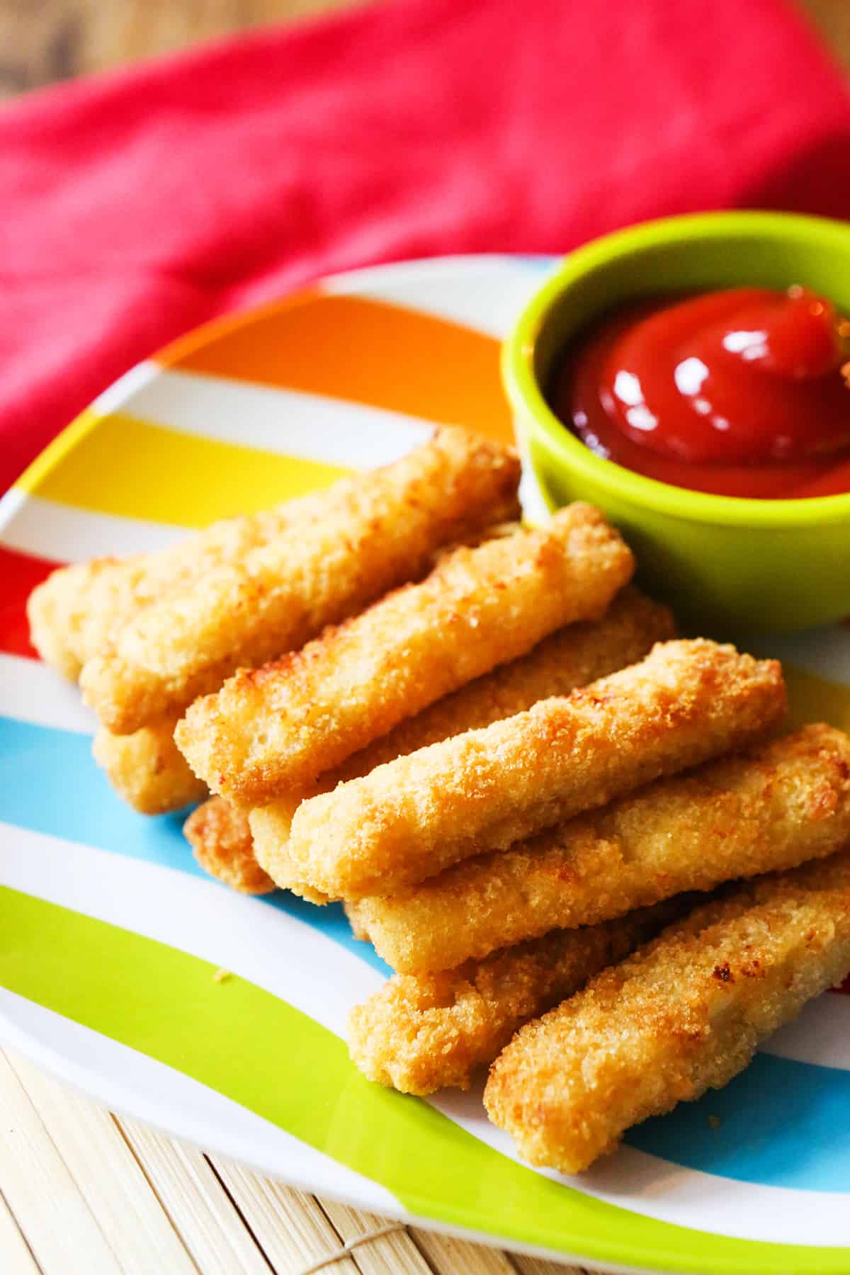 Plate full of stacked fish sticks sitting next to ketchup for dipping.