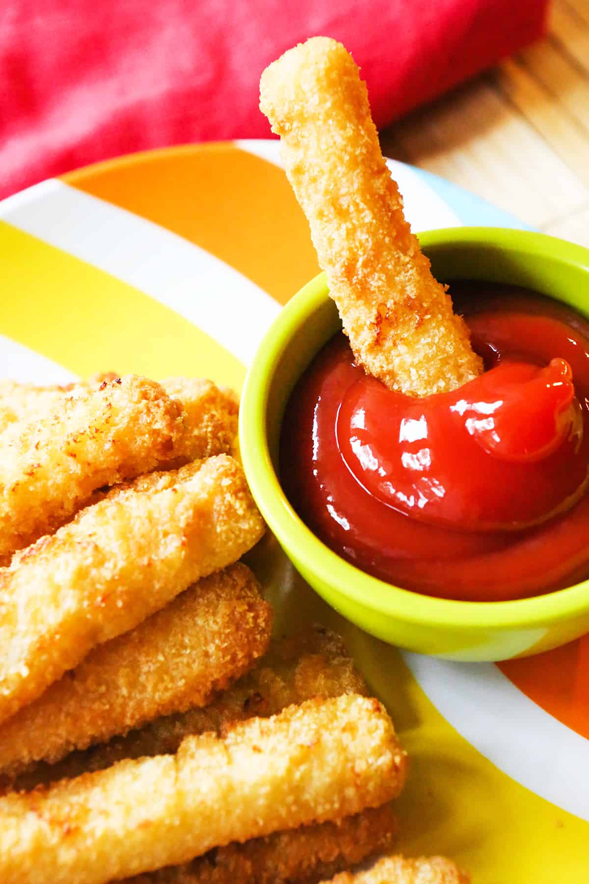A single fish stick being dipped into a small bowl of ketchup.