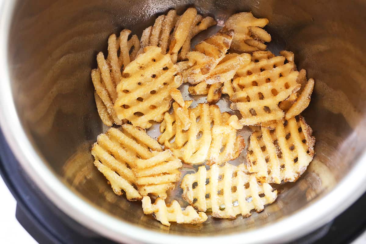 Frozen waffle fries in an air fryer basket.