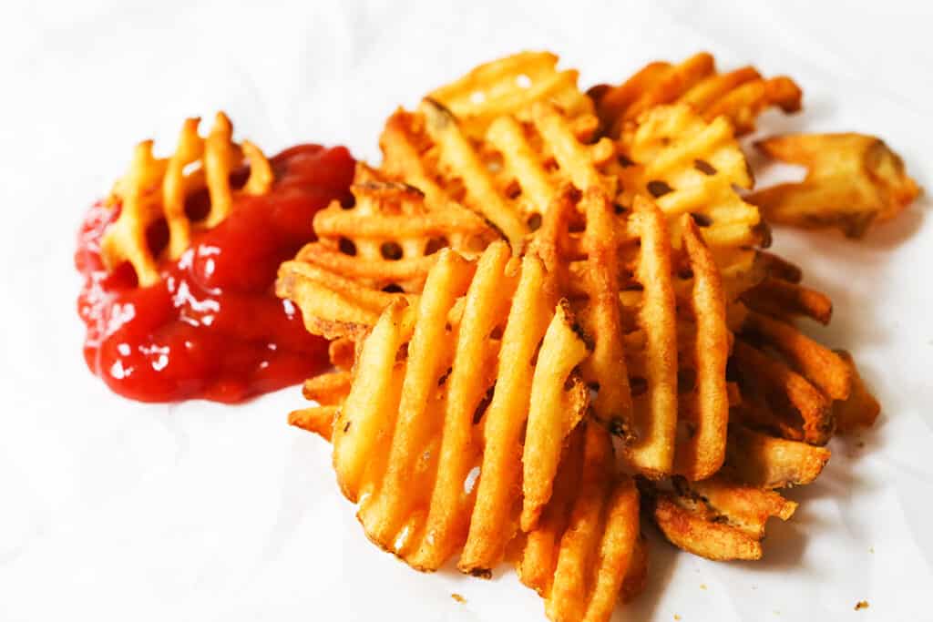 A pile of waffle fries next to some ketchup.