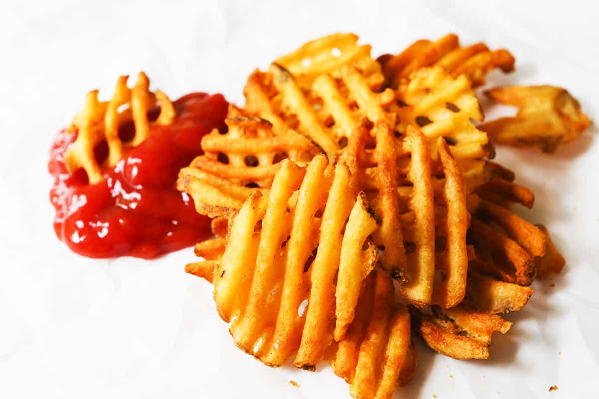 Waffle fries prepared in the air fryer on a plate with ketchup. 