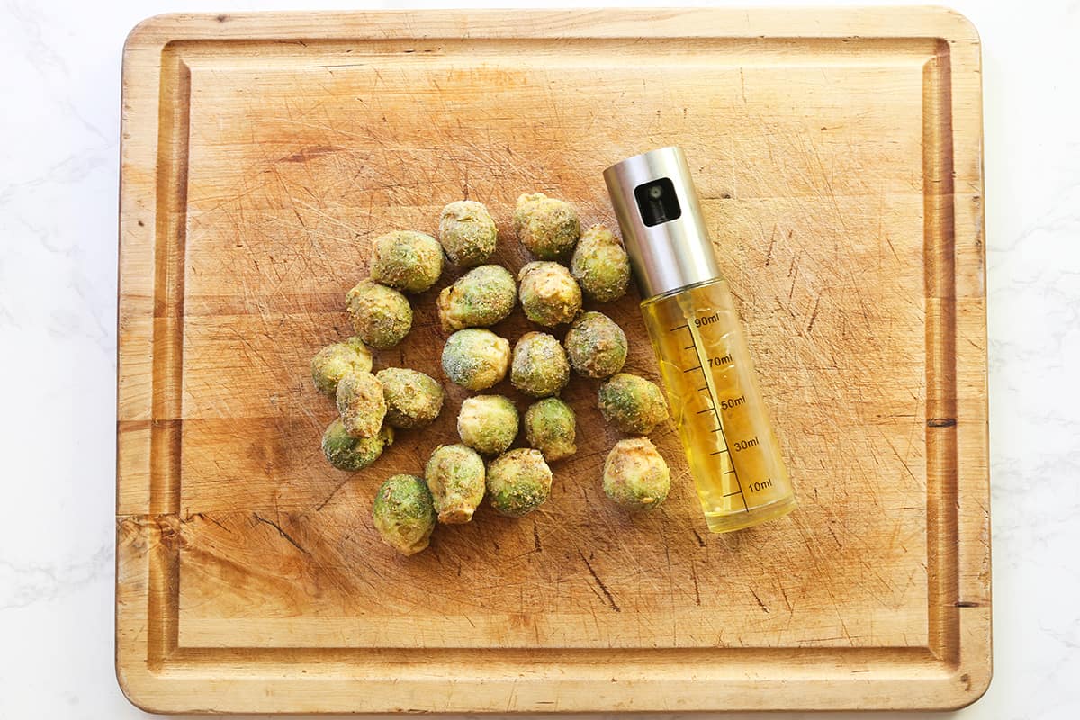 Cutting board with frozen Brussels sprouts and an olive oil spritzer on top.