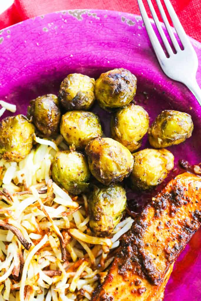 Plate of hashbrowns and brussel sprouts and salmon, ready to eat. 