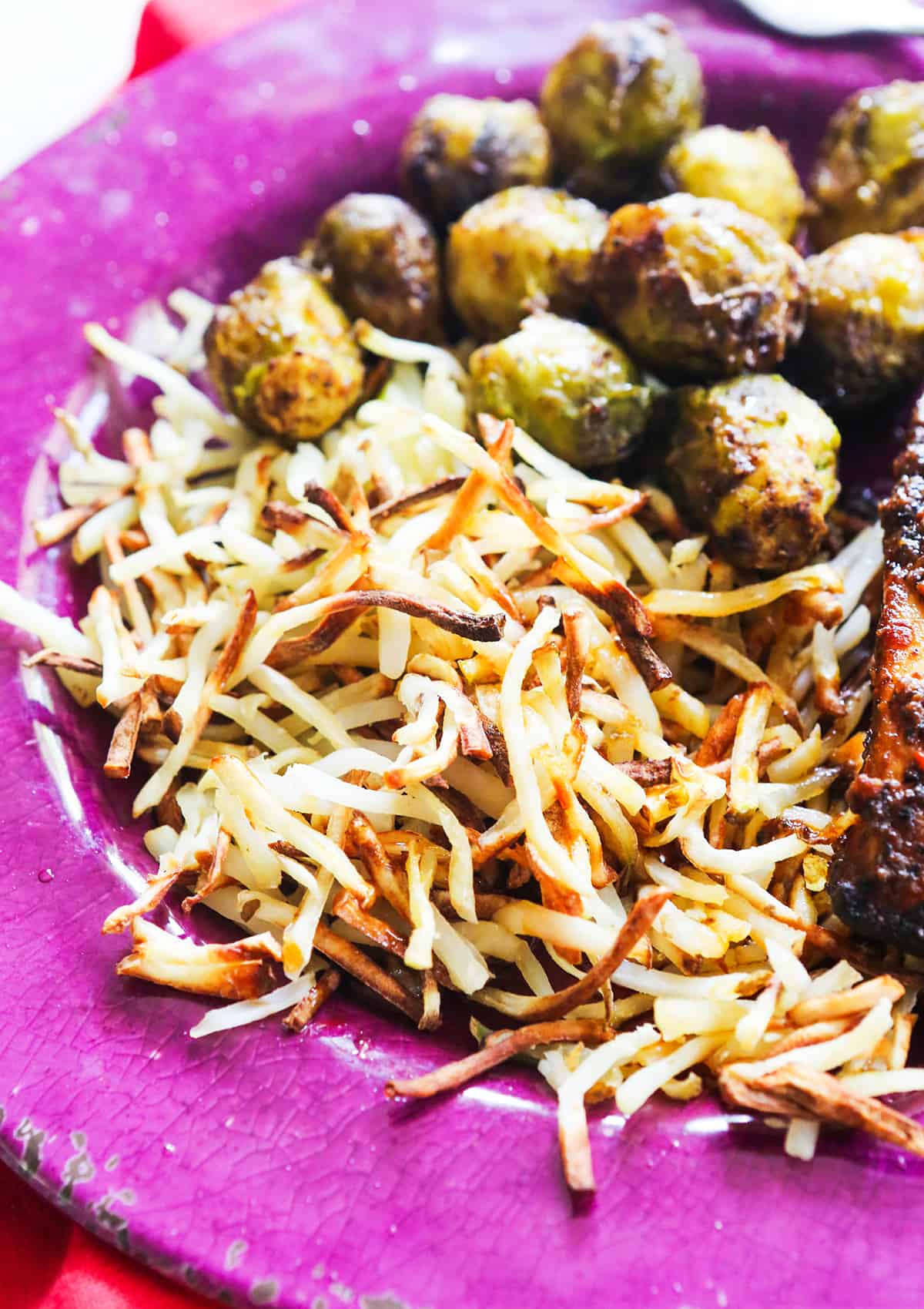 Crispy hash browns on a purple plate next to brussels sprouts.