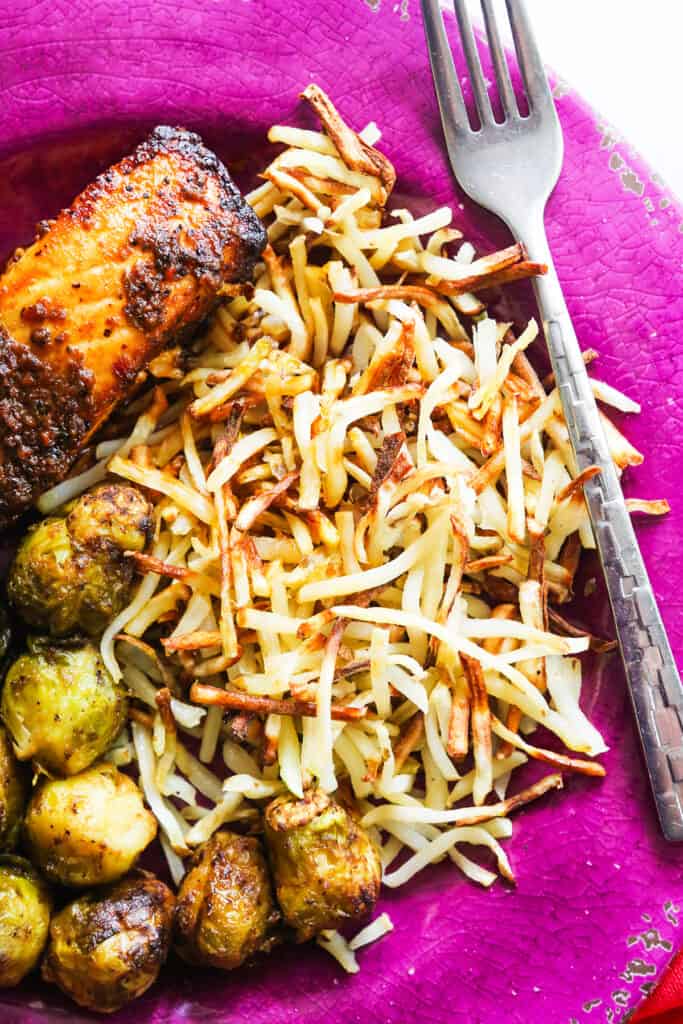 Hash browns on a plate next to brussels sprouts and a slice of salmon. 