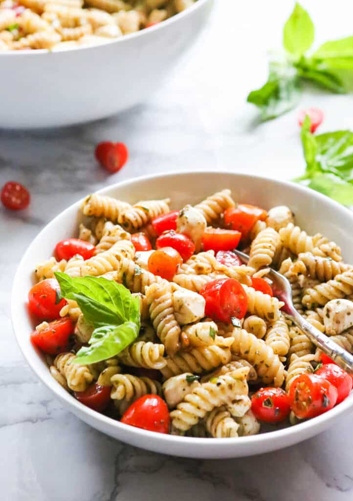 Bowl of caprese pasta salad sitting next to a serving bowl.