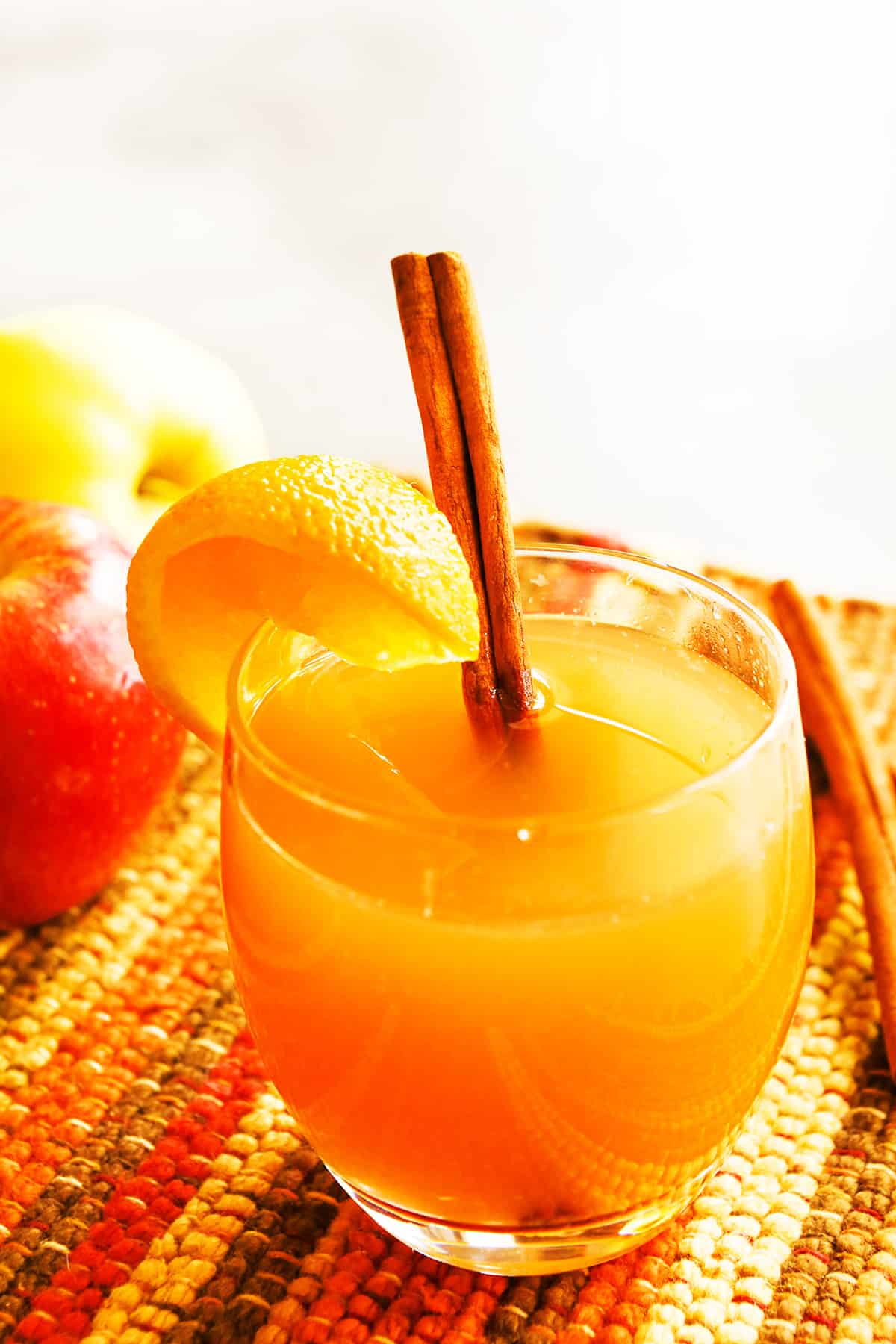 a glass of instant pot apple cider with an orange wedge and a cinnamon stick on the side.