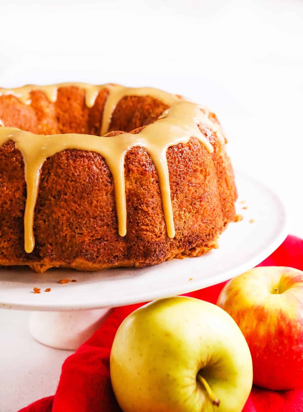 apple bundt cake on a cake display tray with apples underneath it.