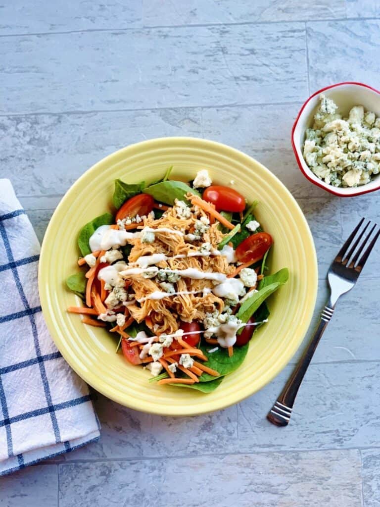 Bowl full of buffalo chicken with a dressing drizzled on top. 