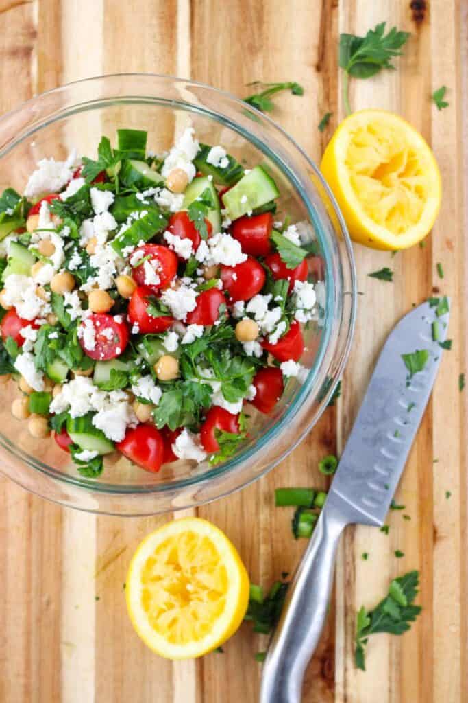 Fresh herb salad in a bowl with feta sprinkled on top and a squeezed lemon on the side. 