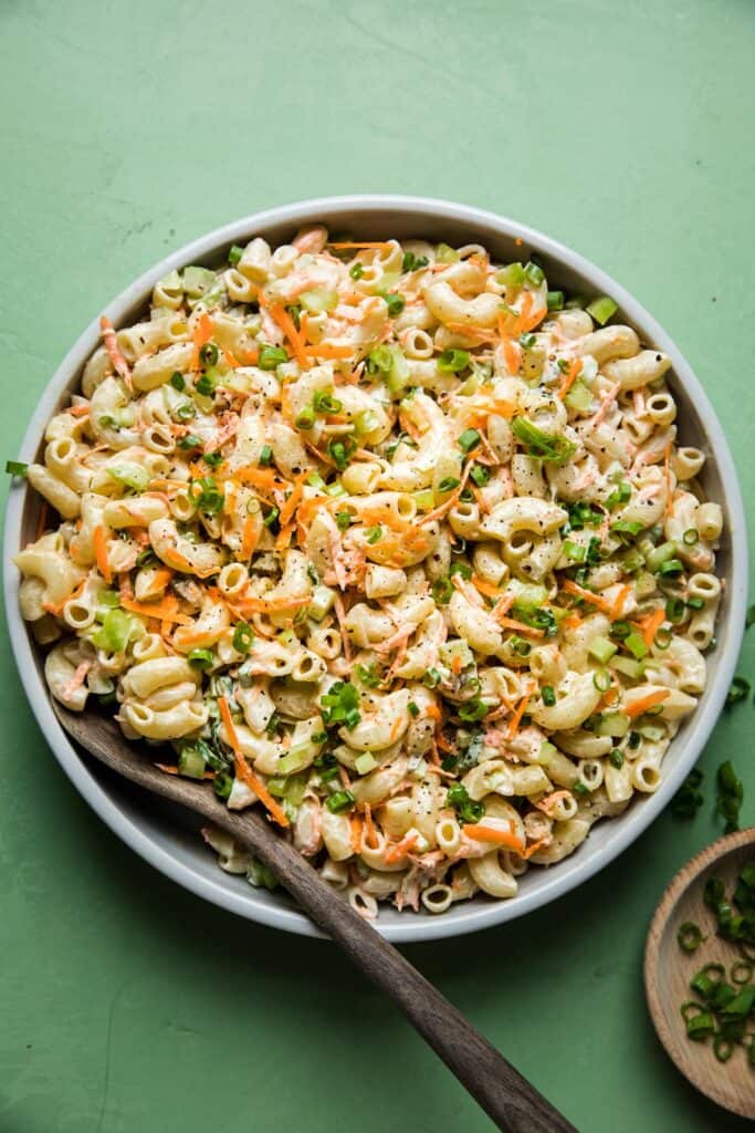 Full serving bowl of macaroni salad with a serving spoon tucked in. 