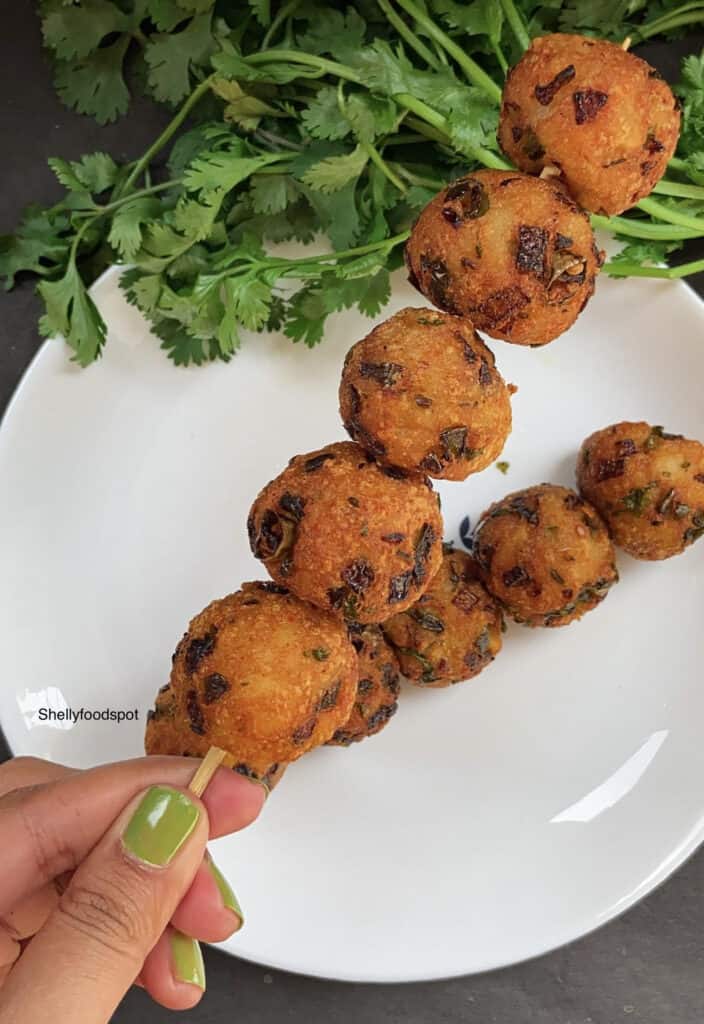 Two spears of crispy potato balls served on a plate with cilantro sprigs alongside. 