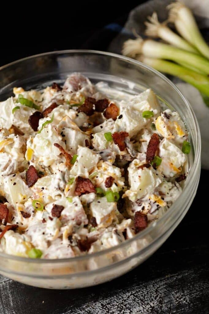 Glass bowl of prepared ranch potato salad with chopped bacon in it. 