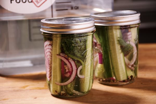 Two jars of canned dill pickles with red onion rounds inside on a table.