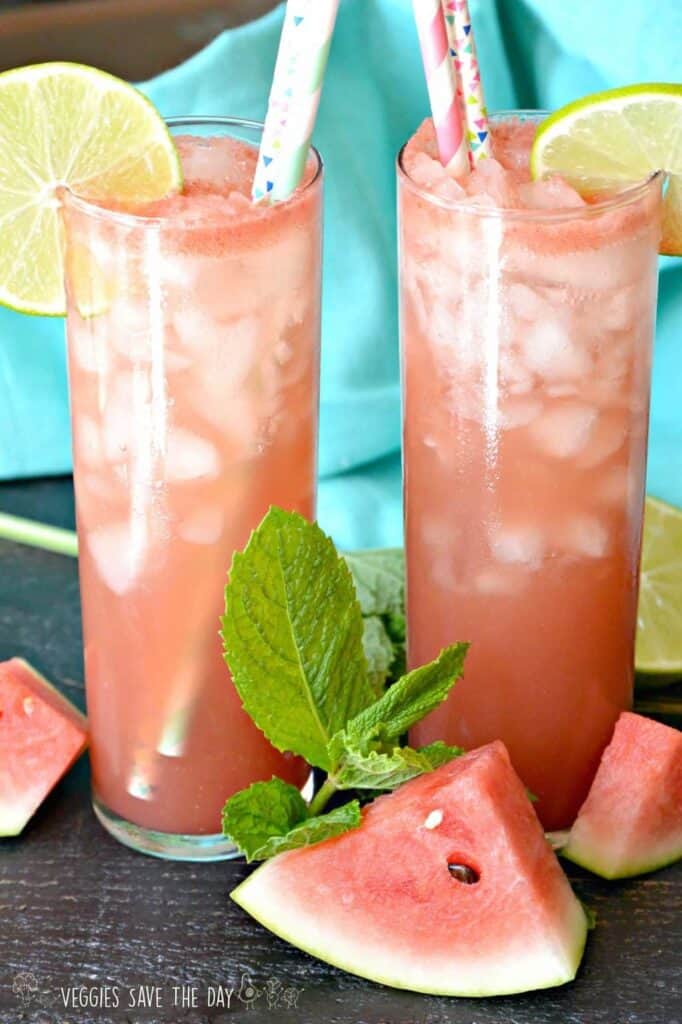 Two tall glasses of watermelon agua fresca with lemon wedges and straws coming out of the drink. 