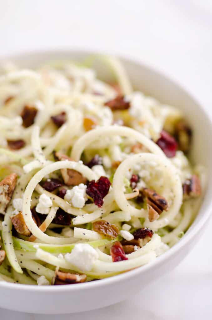A bowl of spiralized apple cranberry salad with pieces of walnuts and goal cheese on top. 