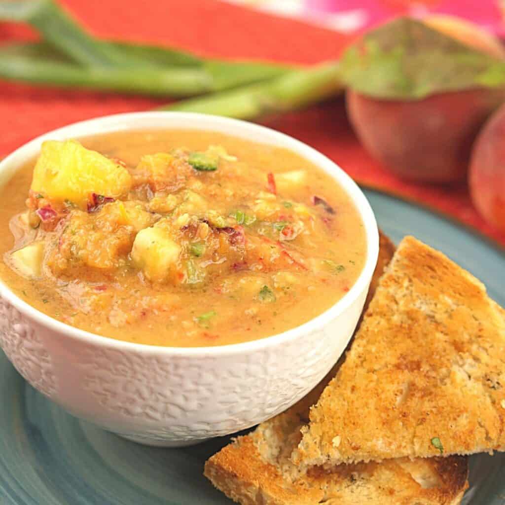 A bowl of watermelon gazpacho on a plate with wedges of toast. 