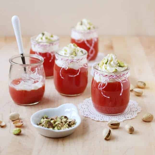 Watermelon pudding in short glass containers topped with whipped cream and crushed pistachios. 
