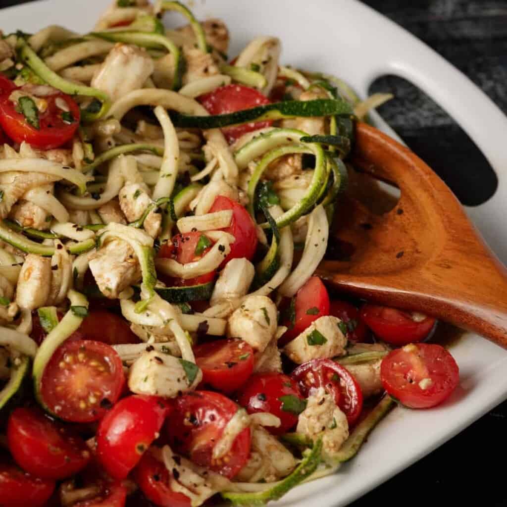 zucchini caprese salad in a serving dish and a wooden serving spoon sticking out. 