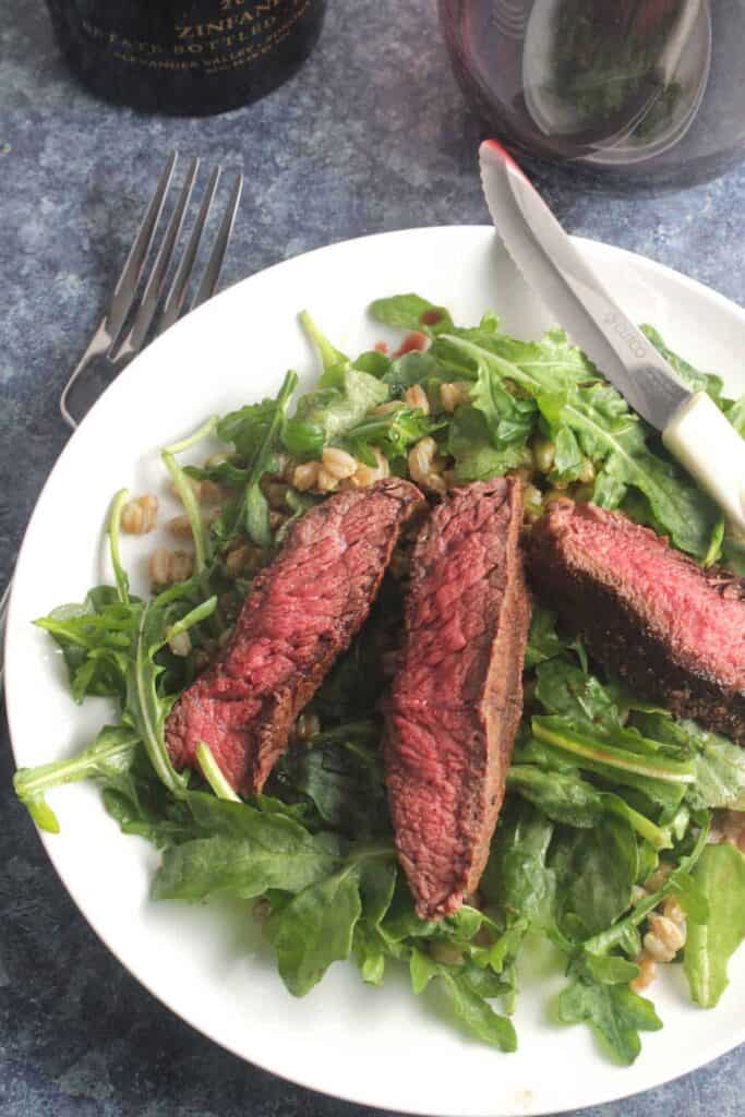 Steak sitting on a bed of arugula ready to serve on a plate. 