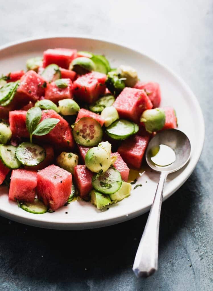 Plate of cucumber avocado watermelon salad with a spoon on the plate. 