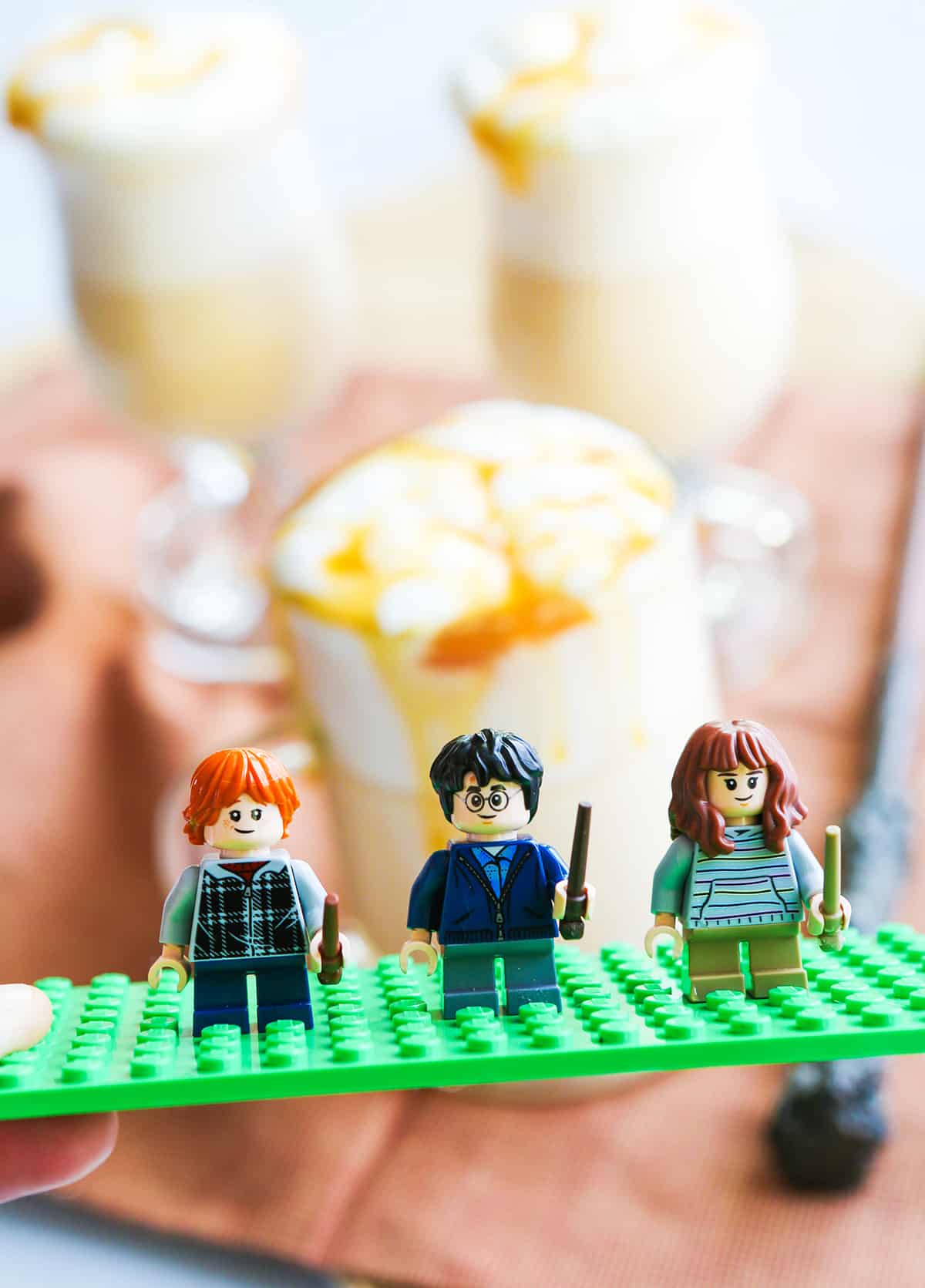 Lego figures of Ron, Harry and Hermione in front of glasses of Butterbeer.