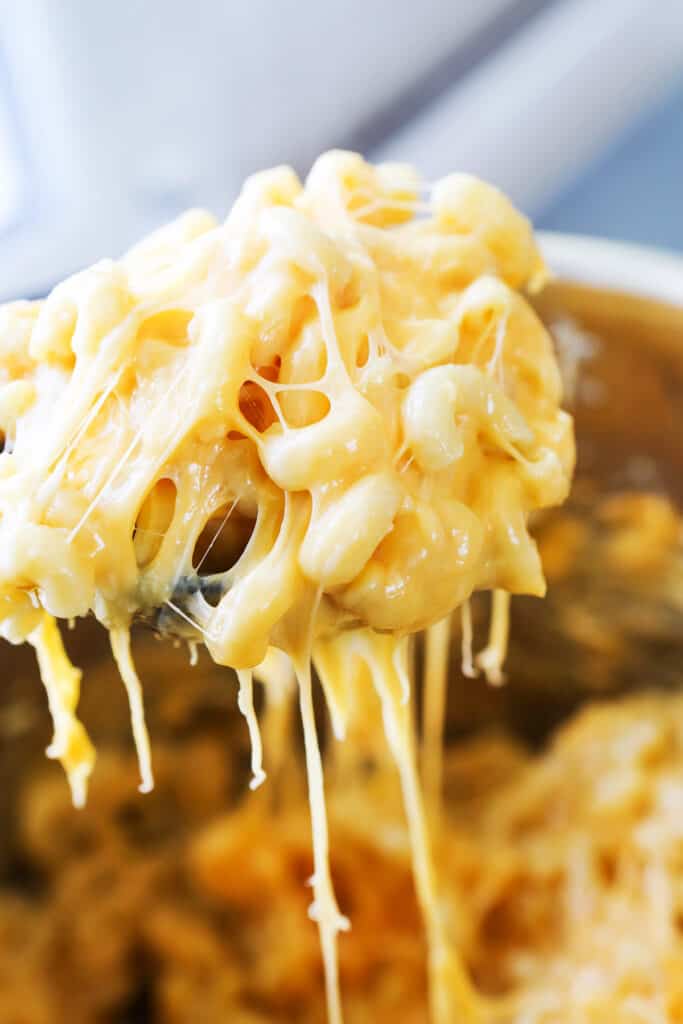 A large scoop of mac and cheese oozing with melted cheese over a pan of the dish. 
