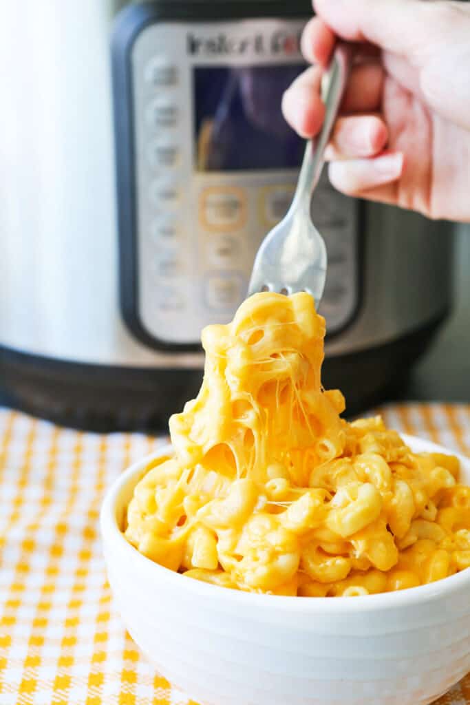 A fork full of creamy mac and cheese in a bowl in front of the instant pot. 