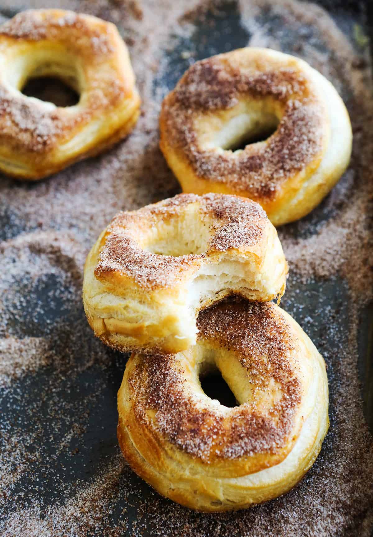 cinnamon sugar air fryer biscuit donuts in sugar mixture, one with bite taken out.