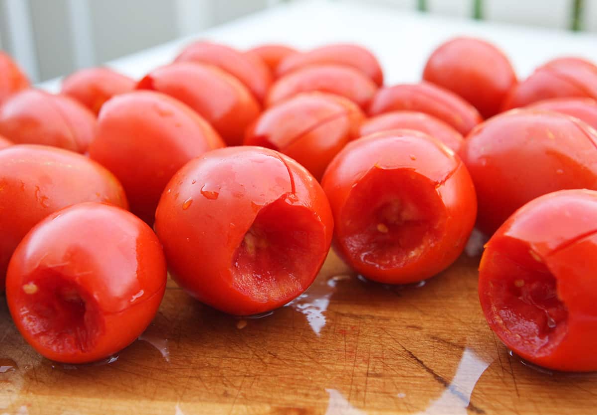 Roma tomatoes lined up on a cutting board with slits cut into the skins.