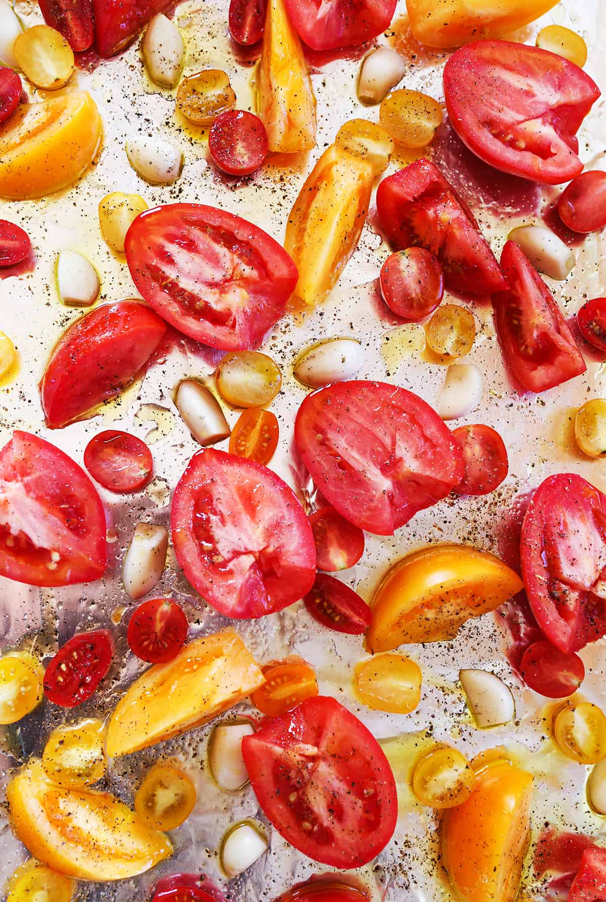 Tomato chunks and garlic pieces on a baking sheet, sprinkled with salt and pepper and ready to bake.