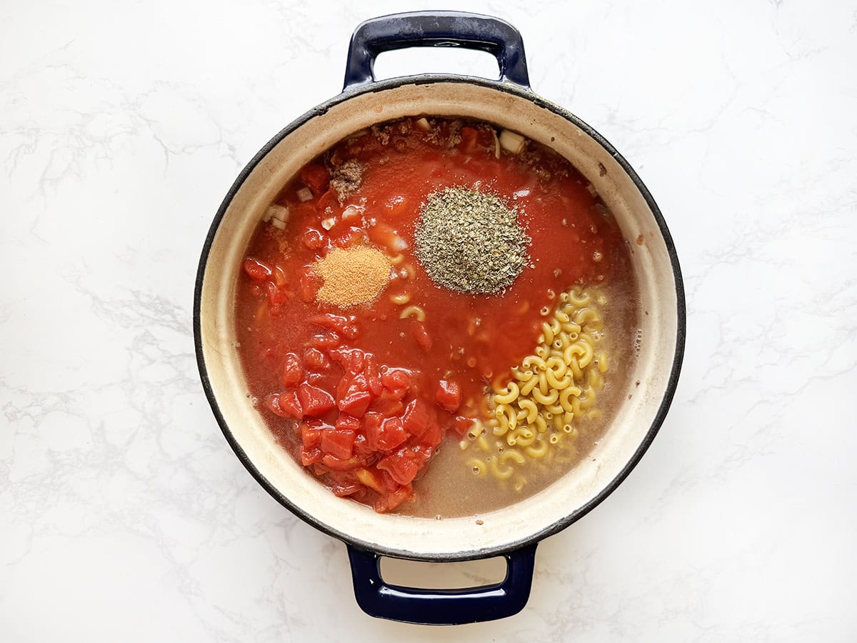Tomato sauce, tomatoes, pasta and seasonings in a Dutch oven, ready to stir and cook.
