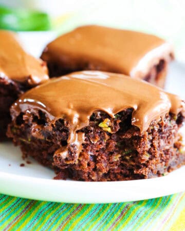 Close-up of chocolate zucchini brownies with peanut butter frosting on a white plate.