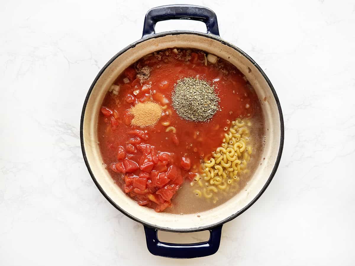 Tomato soup with pasta, diced tomatoes, and herbs in a cooking pot.