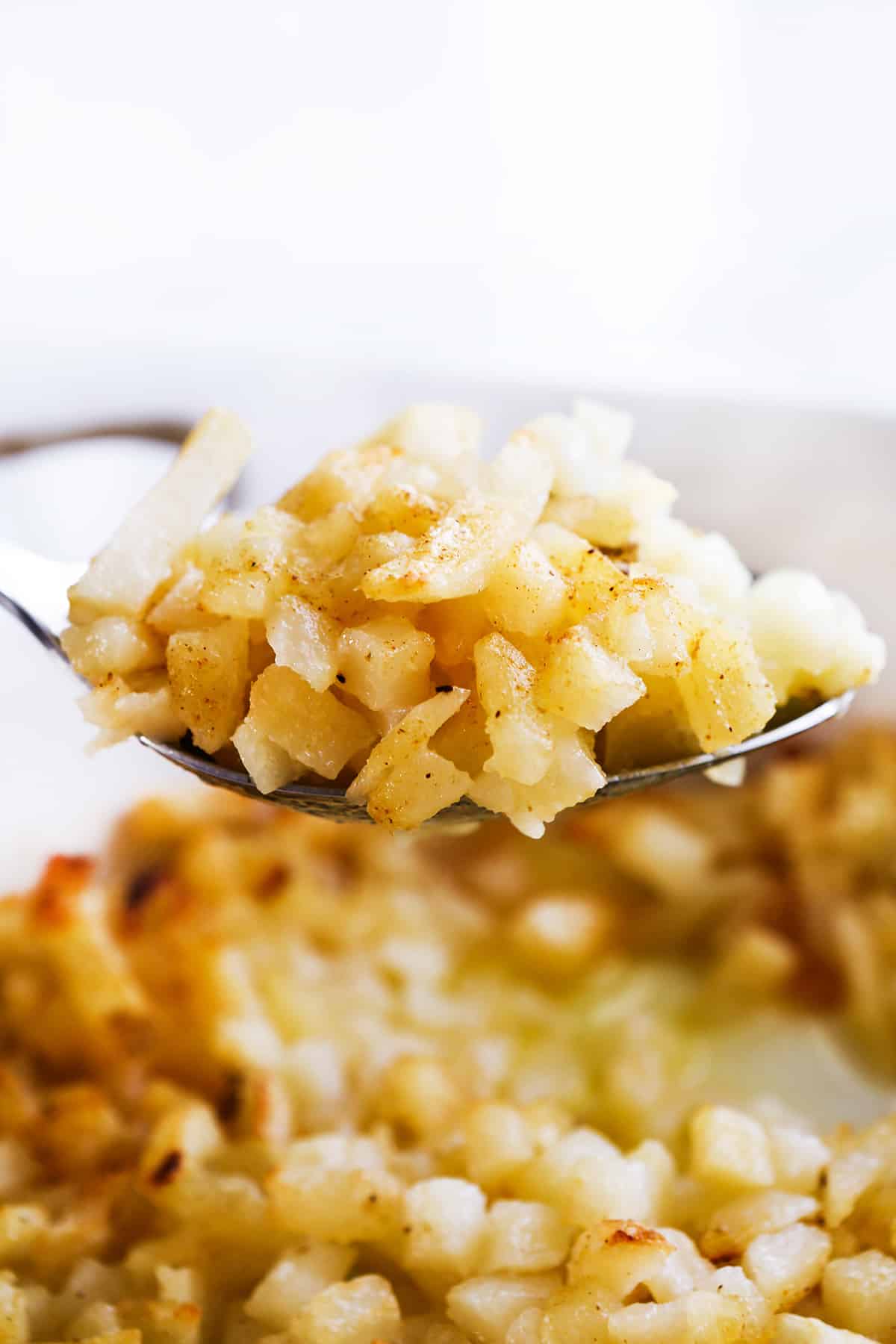 Large spoonful of hashbrown potato casserole hovering over a baking dish.