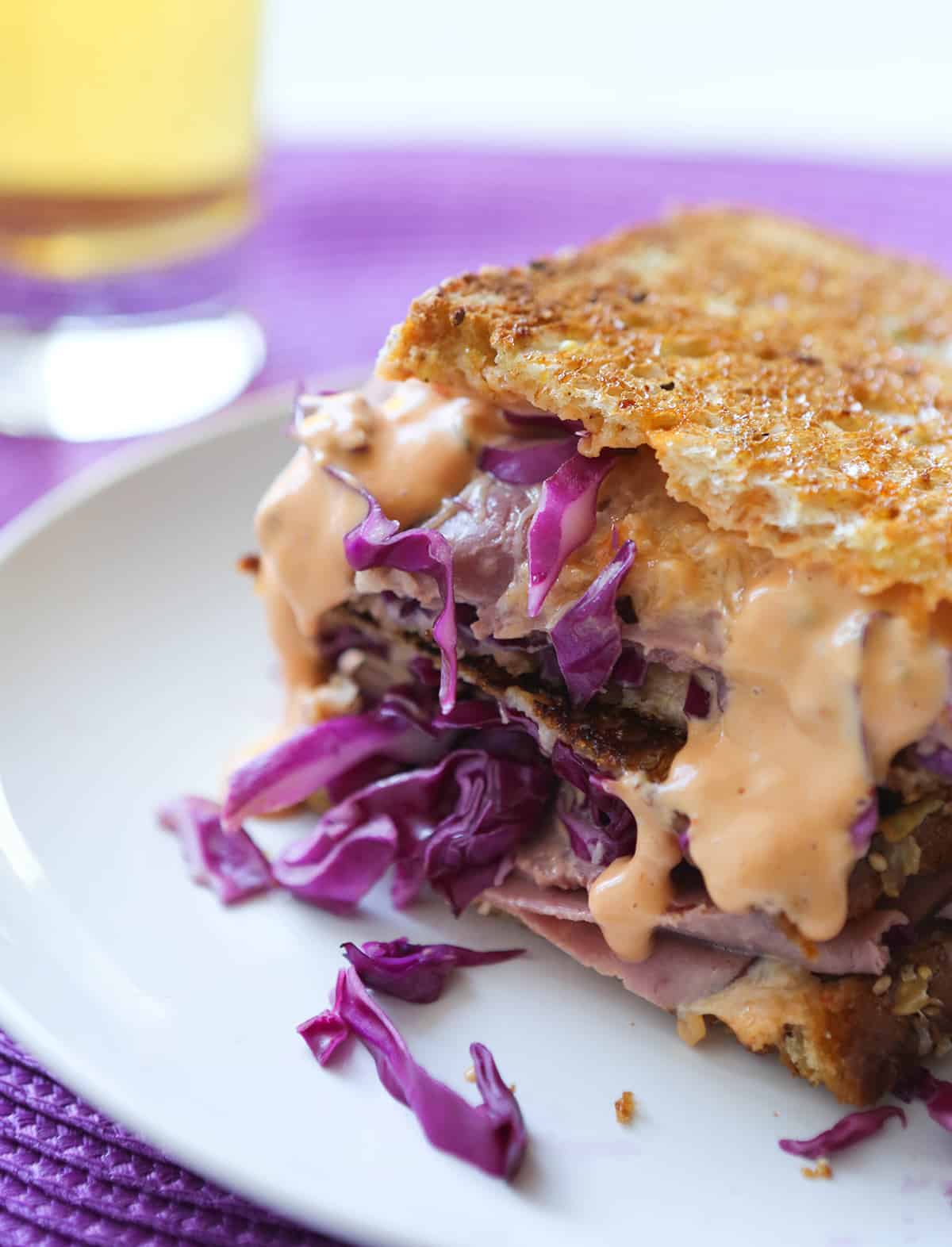 Reuben sandwich on a plate, cut in half, and sitting next to a glass of beer.