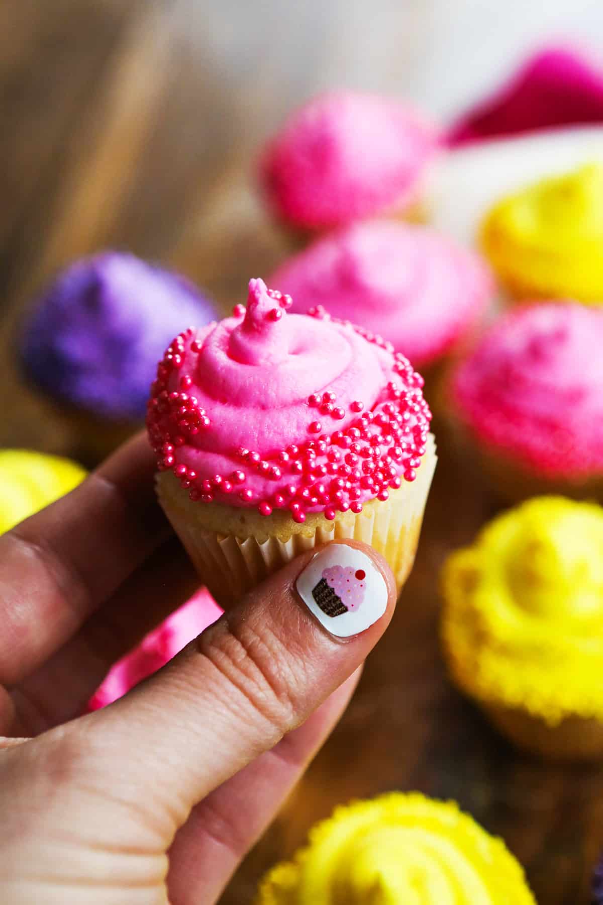 Hand holding a mini cupcake with pink frosting and decor.