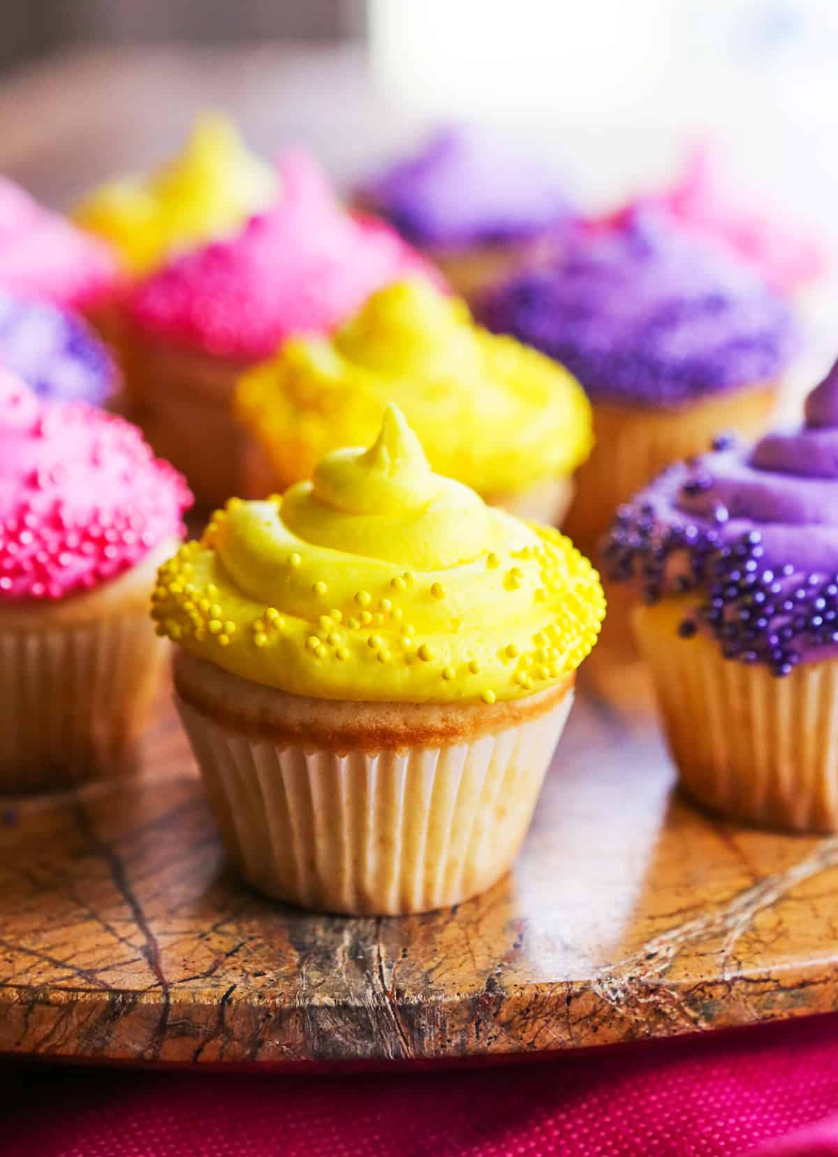White cupcakes with yellow and purple frosting sitting on a serving platter.