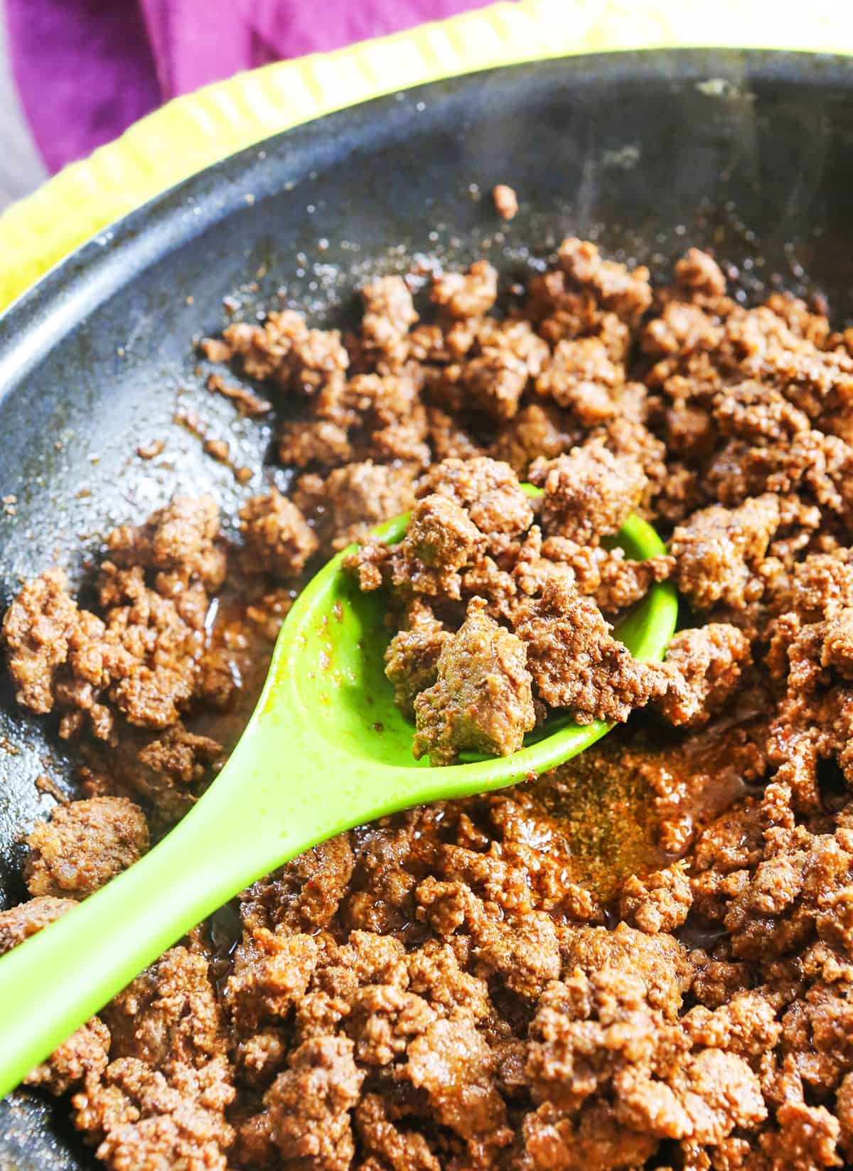 Taco meat in a pan with a green spoon stuck inside.