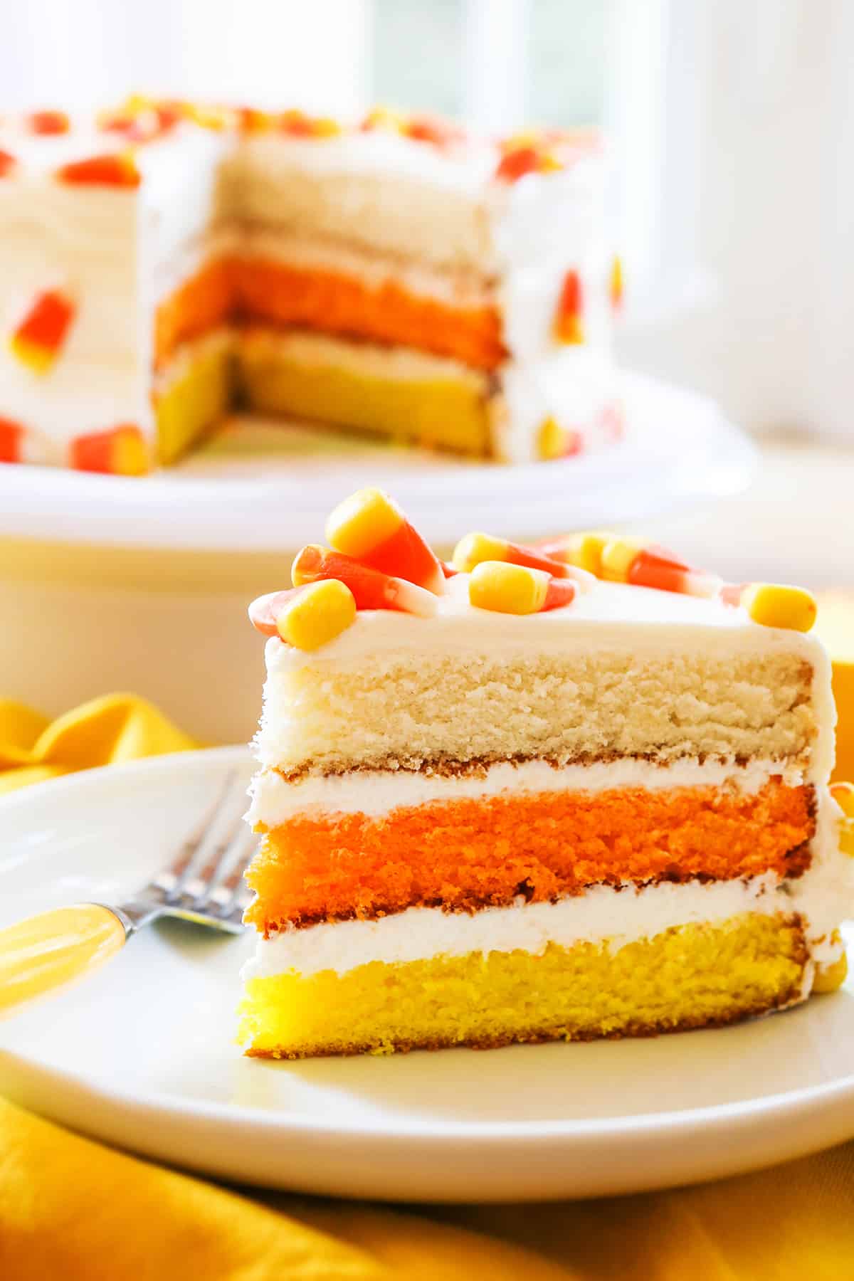 perfect slice of candy corn cake sitting next to cake stand.