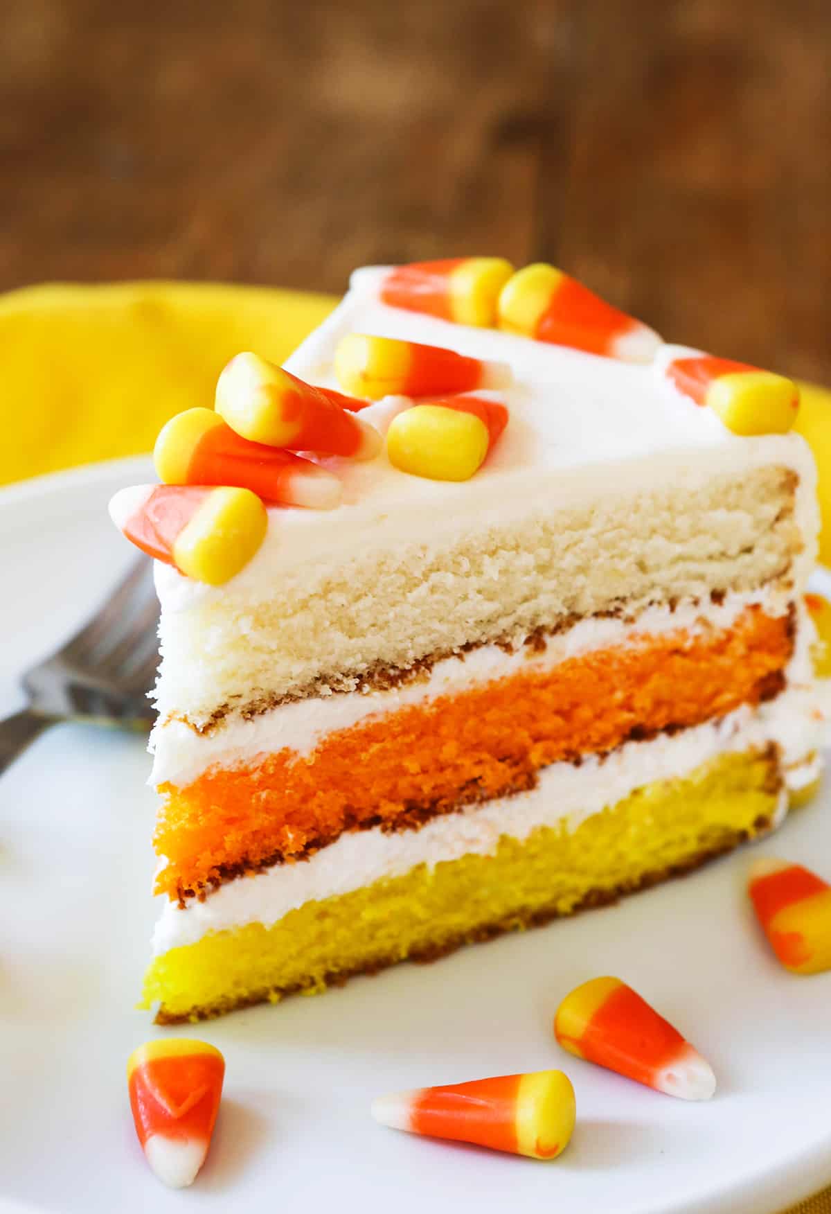 slice of colorful and festive candy corn cake surrounded by candy corn pieces.