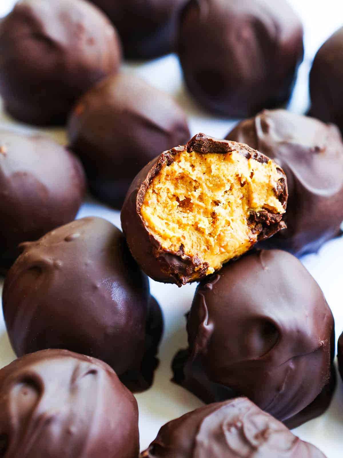 Pumpkin truffles in a stack with the top one having bite removed.
