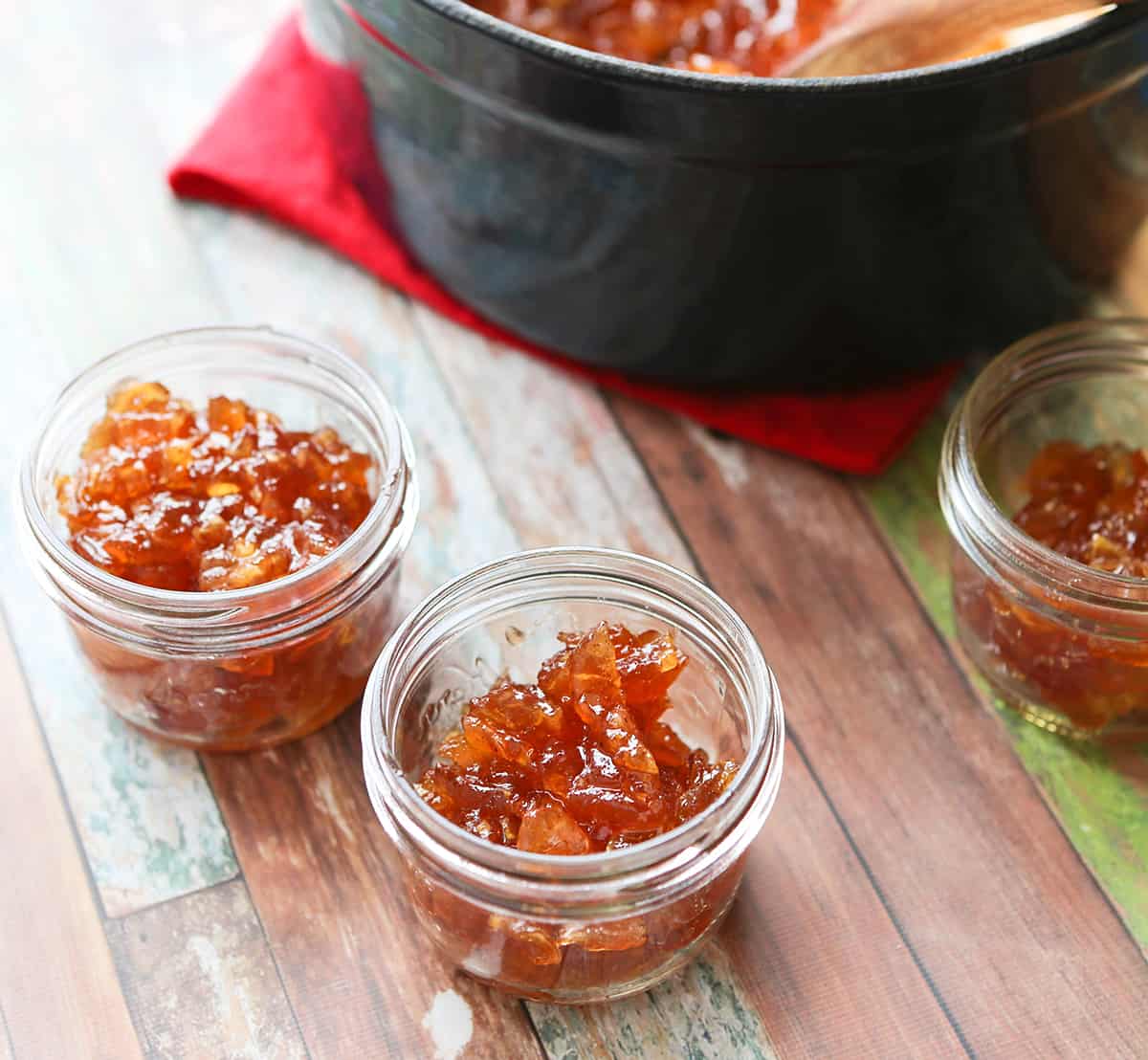 Mason jars filled with apple jam, sitting next to a saucepan.