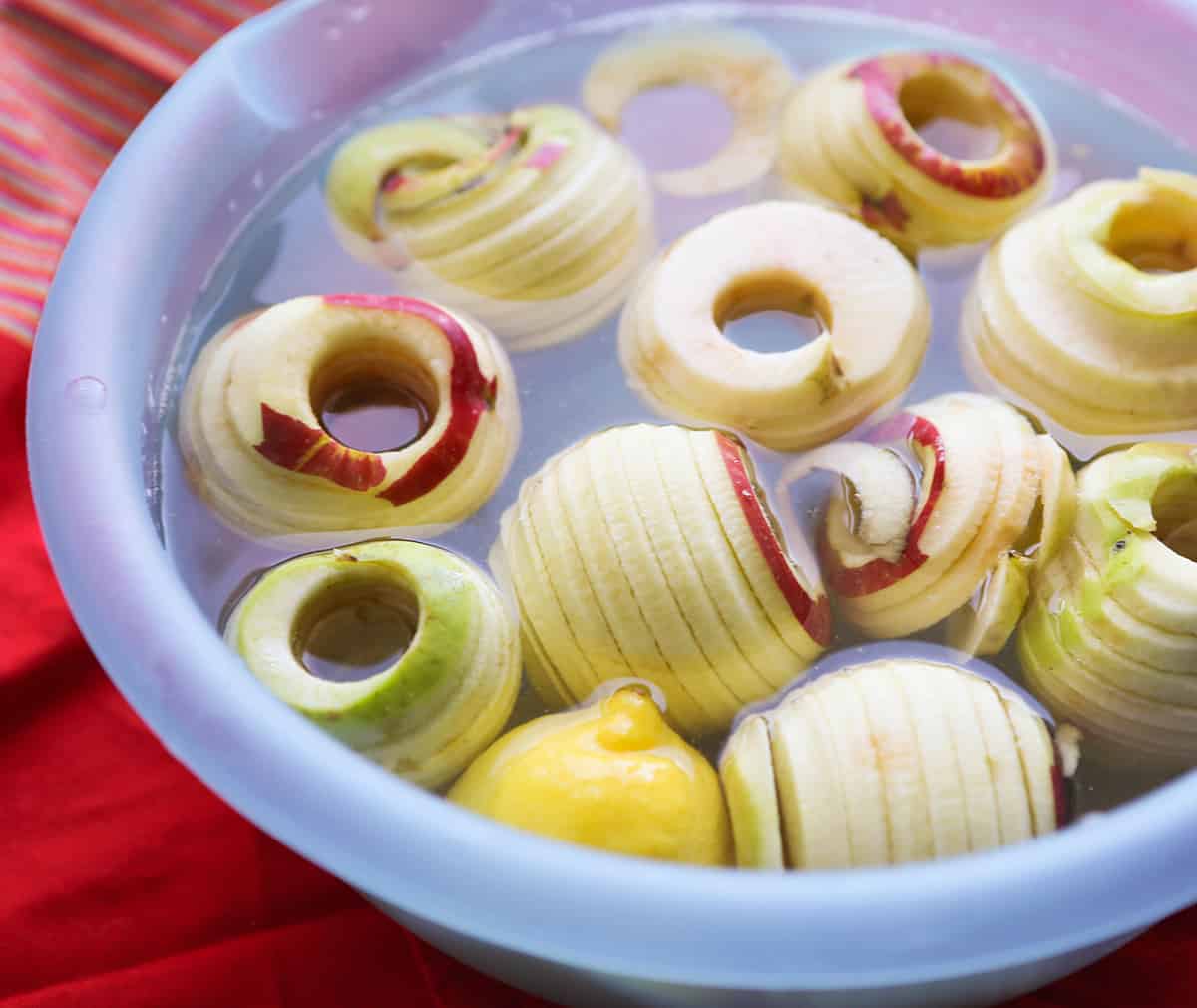 Mixing bowl filled with water and cored, peeled apples.